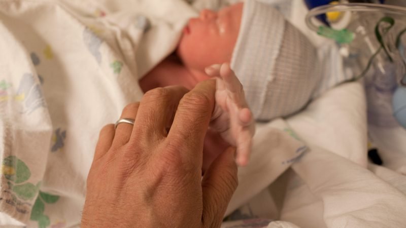 Newborn baby boy gripping parent's finger